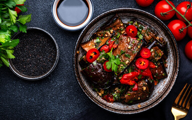 Grilled eggplant with red chili peppers, parsley, sesame seed, soy sauce and garlic in asian style, black table background, top view