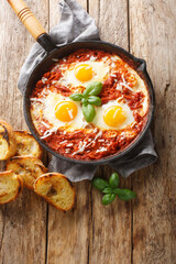 Frying pan with eggs in purgatory closeup on wooden background. Vertical top view from above