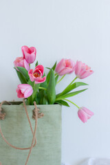 Pink tulips bouquet in green shopping bag on white background copy space