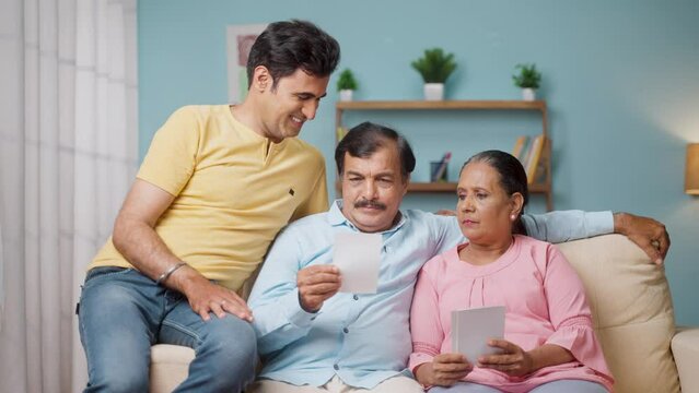 Indian Senior parents showing proposal photos adult son for marriage arrangements at home - concept of responsibility, family caring and parenthood