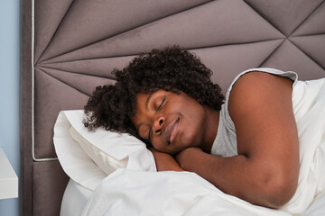 Happy african young woman sleeping on white sheets in bed.