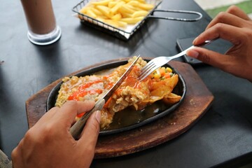 Hand with knives and fork taking beef steak on a hot plate. Left handed.