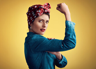 Woman, strong and flexing muscle portrait of a pinup girl in studio for beauty, power and fashion. Female person show bicep on a yellow background for motivation, freedom and retro or vintage style - obrazy, fototapety, plakaty