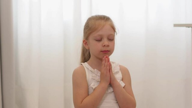 a little girl sits on the floor and prays. The child meditates, repeats mantras. Faith in a miracle. Make wishes, theta meditation.