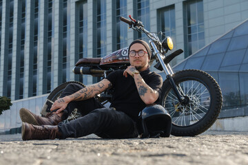 Fototapeta na wymiar Shot of individual motorcycle driver posing near huge city building.