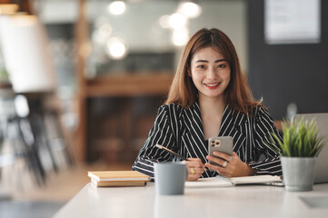Happy businesswoman using mobile phone while analyzing weekly schedule in her notebook.