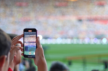A fan recording a football match from the stands with his mobile phone. Selective focus.  © TopMicrobialStock