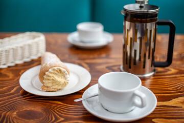 Fresh pastries with filling on the table next to white mugs for coffee or tea for breakfast. Cake for a sweet dessert after lunch at a cozy coffee shop.