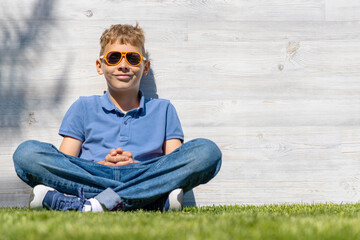Naklejka na ściany i meble A schoolboy in sunglasses sitting on a grassy field