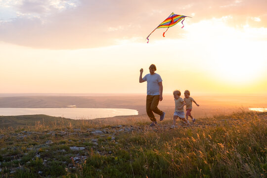 Happy man and children, father and sons, with kite in nature at sunset