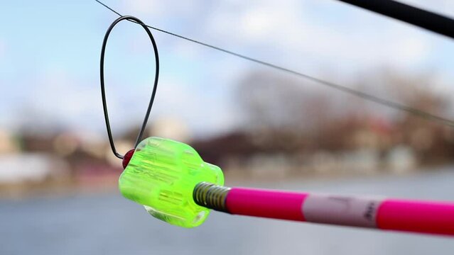 The bite alarm hangs on a fishing rod against the background of water. Fishing rod while fishing on the lake, river. Fishing tackle. Carp rod on a stand with a bite alarm on the line.