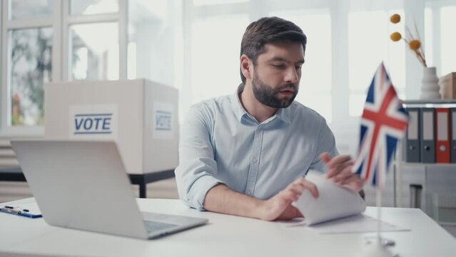 British poll employee working on laptop in office, preparing campaign documents