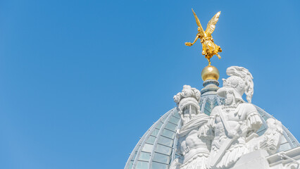 Fototapeta na wymiar Dresden, Germany - May 3, 2023: Banner with old statue of a golden angel and warriors and knights at the dome top in downtown of Dresden, with copy space blue sky solid background.