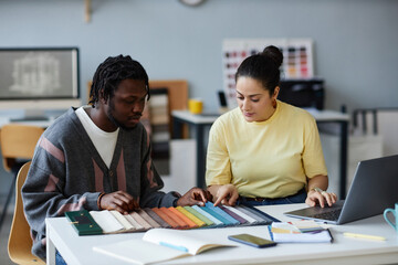 Young colleagues discussing colors on palette while working together in team standing at table in...