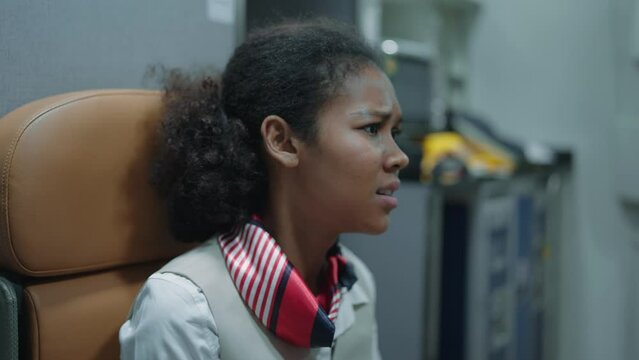Woman african american stewardess, flight attendant sitting on seat panic and worried on flying through storm turbulence