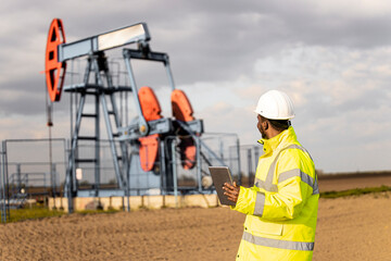 Oil field engineer mechanic monitoring drilling operations on oil rig and holding digital tablet.