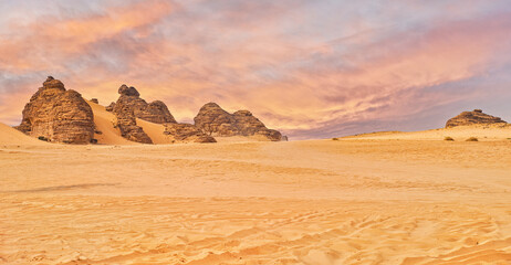 Fototapeta na wymiar Typical desert landscape in Alula, Saudi Arabia, sand with some mountains, small offroad vehicle, dramatic orange sky above