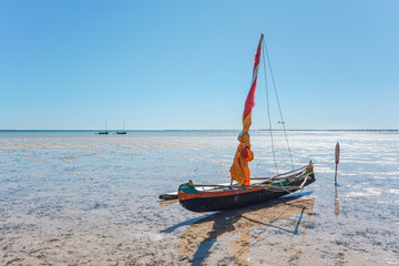 Fisherman piroga (small fishing boat with sail) waiting at the low tide coast on sunny day