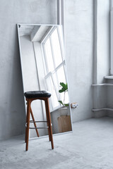 Large framed modern mirror and wooden chair in studio. Vertical view Minimalist interior with concrete wall. Contemporary interior design