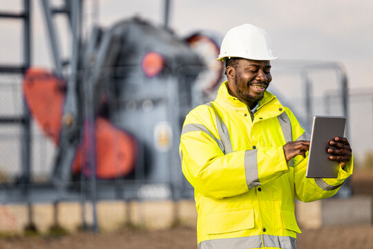 Oil field worker standing in front of the oil rig and working on his digital tablet computer.