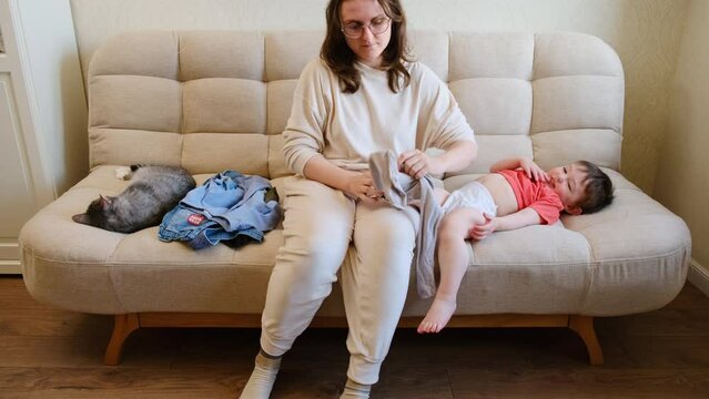 Mother helps child put on clothing for their outdoor adventure. Mom selects soft, breathable clothes for baby boy to wear during walk. Kid aged about two years (one year ten months).