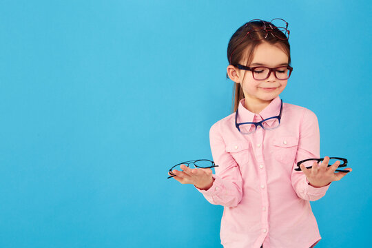 Happy, decision and a girl with optometry glasses isolated on a blue background in studio. Smile, young and a little child with eyewear choice for vision, eyesight and choosing spectacles with mockup