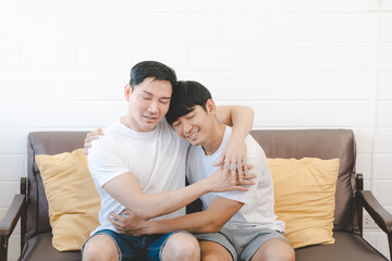 Happy Asian gay couple hug together on sofa. Asian LGBT couple embracing together at home. Diversity of LGBT relationships. A gay couple concept. LGBT multi relationship.