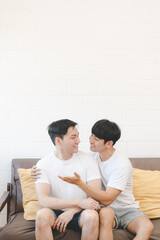 Happy Asian gay couple hug together on sofa. Asian LGBT couple embracing together at home. Diversity of LGBT relationships. A gay couple concept. LGBT multi relationship.