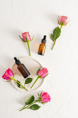 Two cosmetic bottles with dropper with a multifunctional serum on a white background with fresh roses. Top view. Flat lay. natural cosmetics.