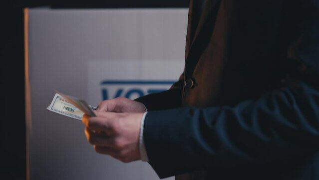 Politician in business suit counting money, ballot box background, corruption