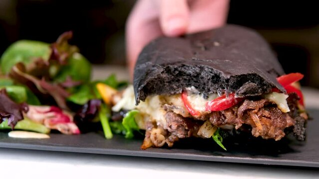 black bread bun with cuttlefish ink sandwich cheeseburger hamburger restaurant serving with salad on black plate near window delicious appetizing bulgogi, spicy bulgogi, house-made, squid inc bread