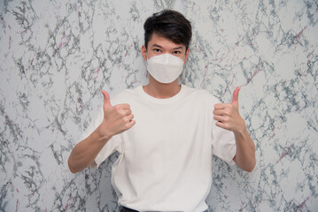 Young Man puts on a face mask showing thumbs up and looking serious isolated on White background,protecting from virus during quarantine.Covid-19