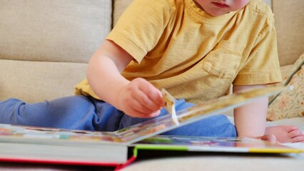 The baby happily tore off a page from the cute picture book while learning to read. The child was reading the book with a finger running through the leaf when suddenly a page got torn off.
