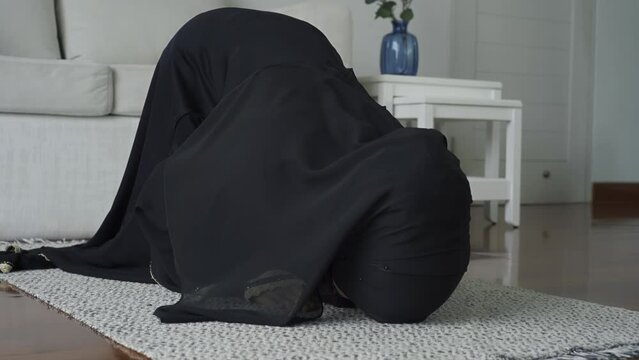 An Asian Muslim woman reciting Salah or Salat al-Fatiha passage of the Qur'an, in a single act of sujud called a sajdah or prostrations at home