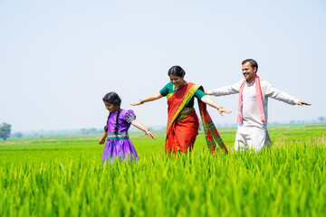 Playful Happy village farming couple with kid walking at green farmland by balancing - concept of real people, family bonding and enjoyment