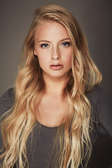 Naklejka premium Face, beauty and portrait of a woman in studio with makeup, cosmetics and long hair. Headshot of a female aesthetic model with a natural glow, luxury skincare and seductive pose on a grey background