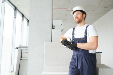 Portrait of positive, handsome young male builder in hard hat. - obrazy, fototapety, plakaty