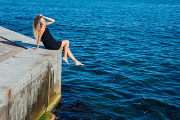 a woman sitting on a pier near the sea walking the beach