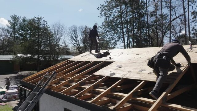 Home building construction workers installing roof sheathing on new home rooftop