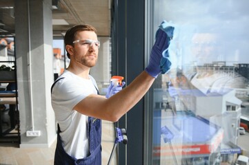 Male professional cleaning service worker in overalls cleans the windows and shop windows of a store with special equipment.