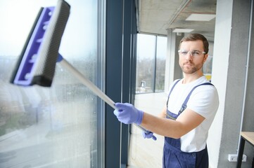 Male professional cleaning service worker in overalls cleans the windows and shop windows of a...