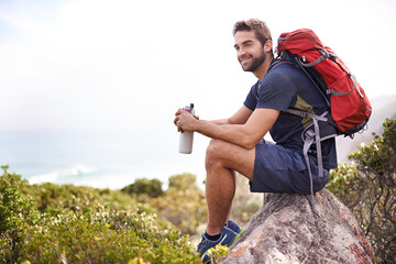 Hiking, mountain and man rest on a rock thinking after exercise, workout and fitness in nature for wellness. Travel, vacation and male person or athlete smile at a view after training and trekking