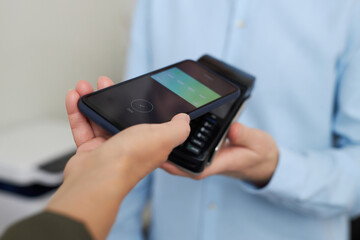 Closeup of unrecognizable woman paying via smartphone NFC technology in shop or clinic, copy space