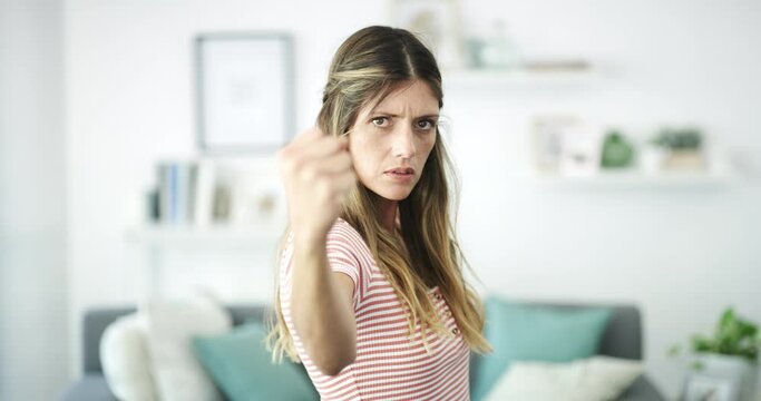 Woman, serious face and threat with fist, punch or aggressive warning in angry, frustrated or fight movement, home or living room. Girl, portrait and mad fighting, pose or gesture of violence
