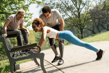 Obraz premium Young people workout at the park. Blonde female doing push-ups and her female friends cheering her up. 