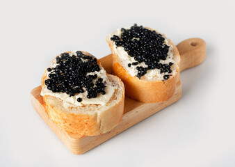 pieces of baguette with butter and halibut caviar on a wooden board on a white background