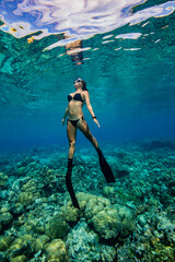Young Asian woman in bikini swims in tropical waters above coral reef