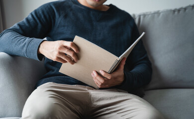Man reading the notebook sitting on the sofa at home.