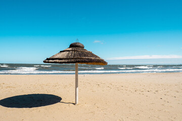 Straw beach rattan parasol at the empty beach with blue sky backgrounds sea ocean coast. Relaxing...