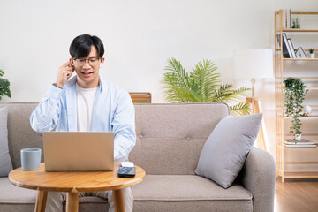 Focused young asian businessman wear headphones study online watching webinar podcast on laptop listening learning education course conference calling make notes sit at work desk, elearning concept